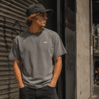 Person iført grå Endless Hope T-shirt med lille reflekslogo på brystet. T-shirten har et minimalistisk design og er fotograferet i urbane omgivelser.