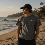 Person iført grå Endless Hope T-shirt med lille reflekslogo på brystet. T-shirten er fotograferet ved stranden med havet i baggrunden og afspejler en afslappet livsstil inspireret af kysten.