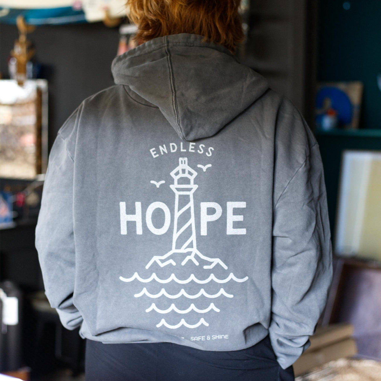 Grå hoodie med stort HOPE refleksprint og fyrtårnsmotiv på ryggen