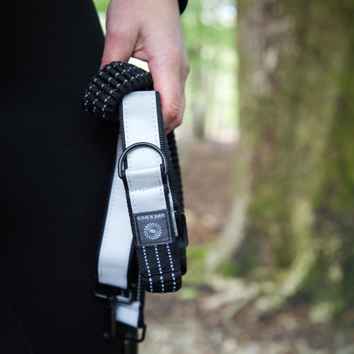 Refleksstrop fra Safe & Shine med elastisk sort rem og refleksdetalje holdt i hånden i naturen