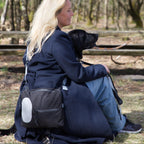 Kvinde med hund i naturen bærer sort skuldertaske med refleksdetalje fra Safe & Shine – synlighed til hverdag og gåture