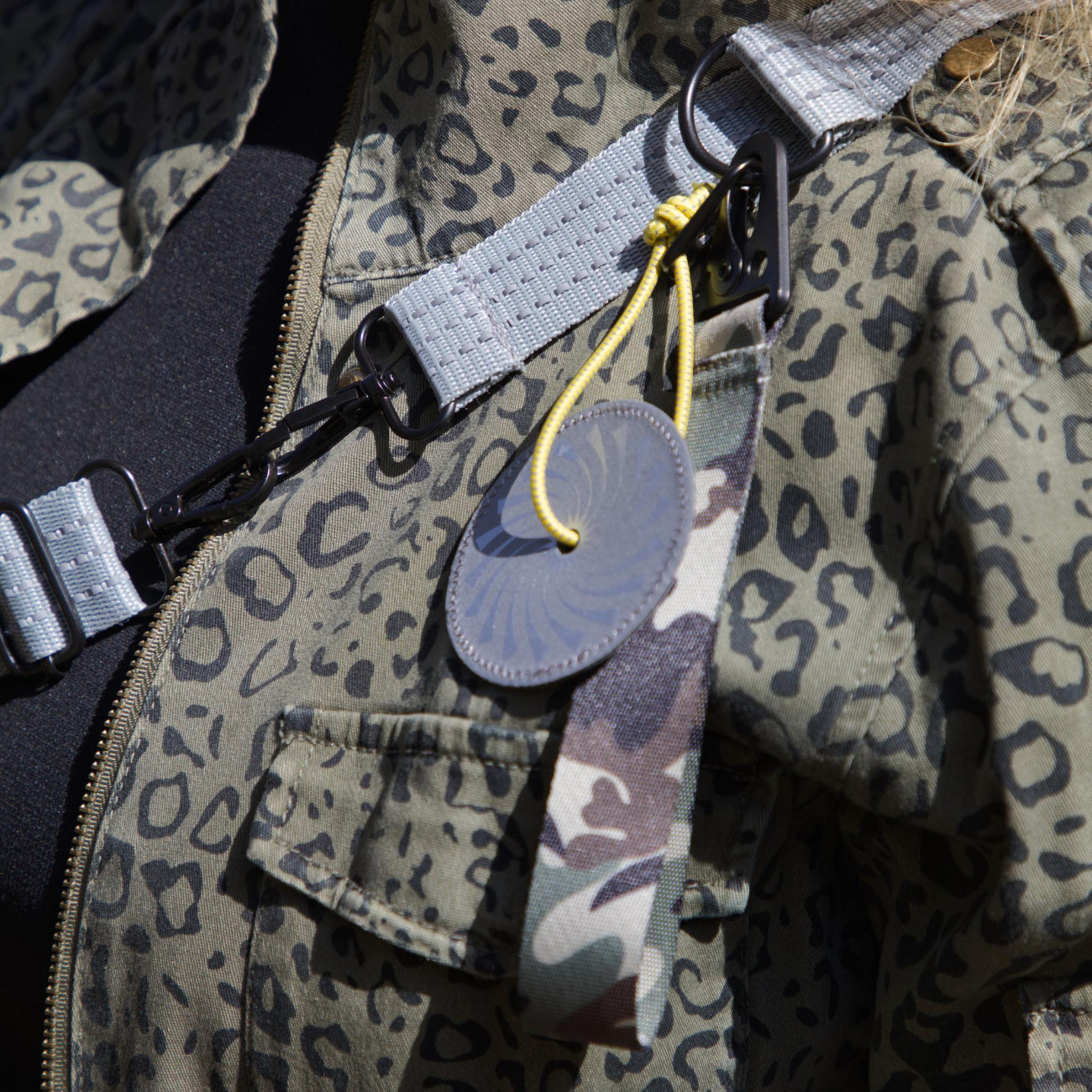 Refleksvedhæng fra Safe & Shine fastgjort på taske med gul refleksnor og camouflage rem