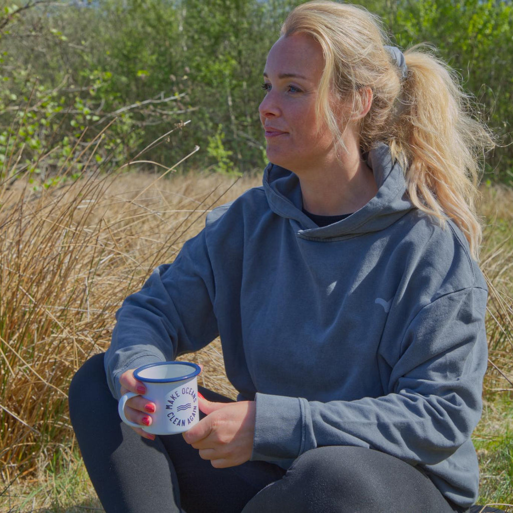 Kvinde sidder i naturen med kop og grå hoodie med diskret reflekslogo fra Safe & Shine – komfort og synlighed i hverdagen
