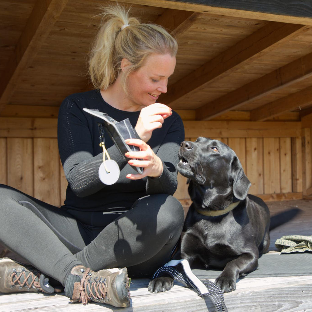 Kvinde med sort hund bruger Galaxy taske og refleksvedhæng fra Safe & Shine under pause i naturen