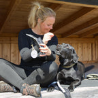 Kvinde med sort hund bruger Galaxy taske og refleksvedhæng fra Safe & Shine under pause i naturen