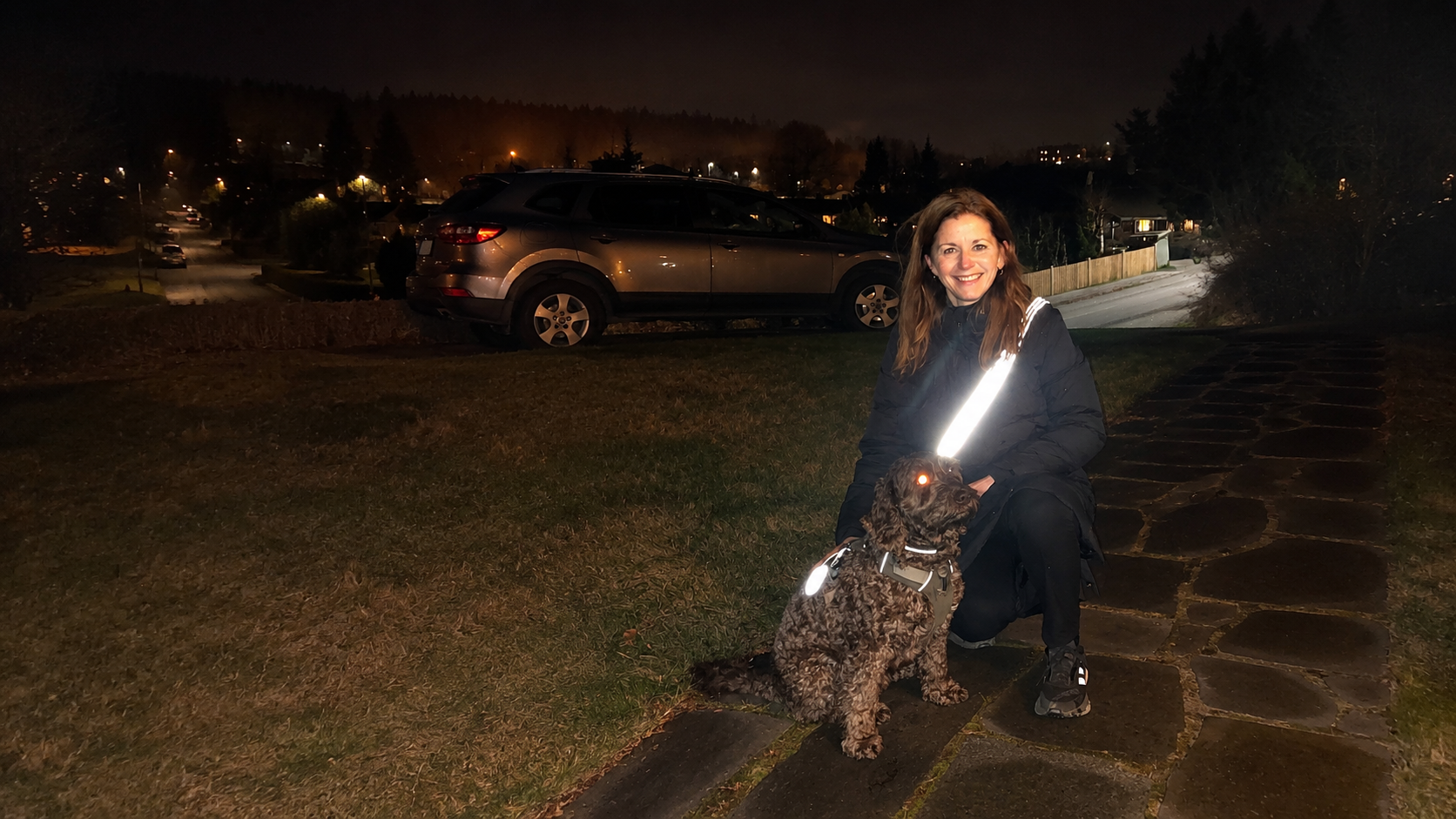 Kunde og hund på gåtur efter mørkets frembrud med Safe & Shine refleksprodukter, der øger synligheden i trafikken.