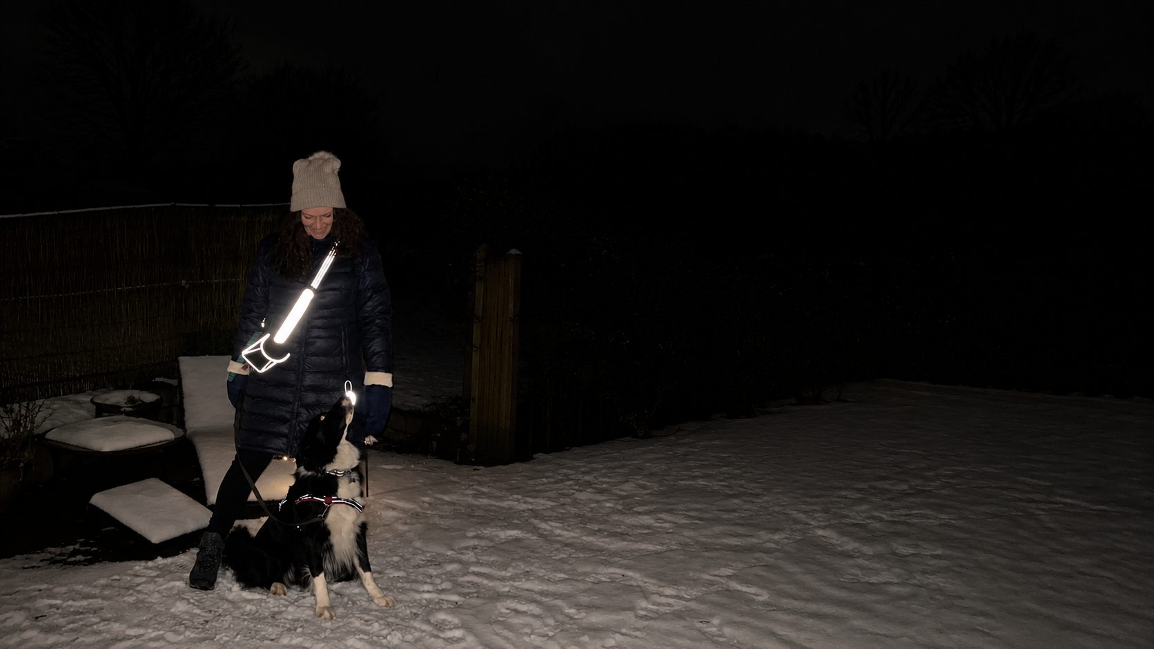 Kvinde og hund på aftengåtur med Safe & Shine refleksprodukter. Comet refleksstrap og Neptun refleksvedhæng giver ekstra synlighed og sikkerhed i mørket.